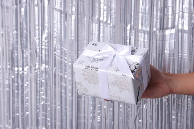 Photo of Man with gift box near silver foil curtain against light background, closeup. Space for text