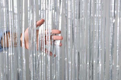 Photo of Man near silver foil curtain against light background, closeup