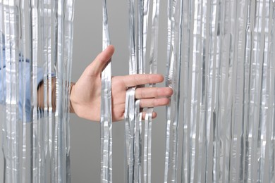 Photo of Man near silver foil curtain against light background, closeup