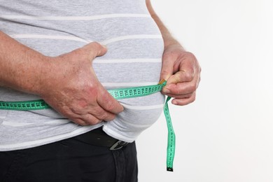 Photo of Overweight man measuring his belly with tape on white background, closeup. Space for text