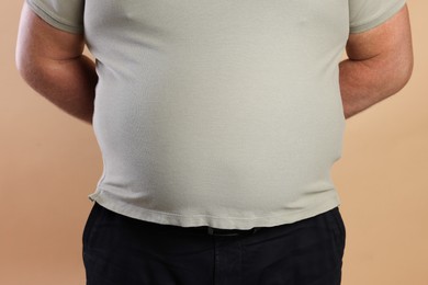 Photo of Overweight man in tight t-shirt on beige background, closeup