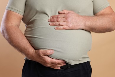 Photo of Overweight man in tight t-shirt on beige background, closeup