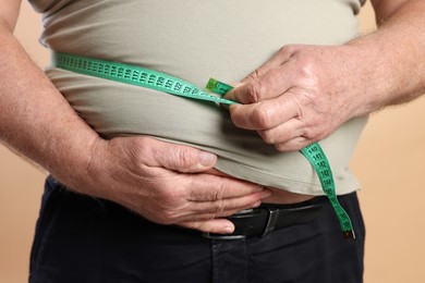 Photo of Overweight man measuring his belly with tape on beige background, closeup