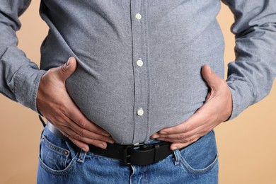 Photo of Overweight man in tight shirt on beige background, closeup