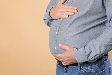 Photo of Overweight man in tight shirt on beige background, closeup. Space for text