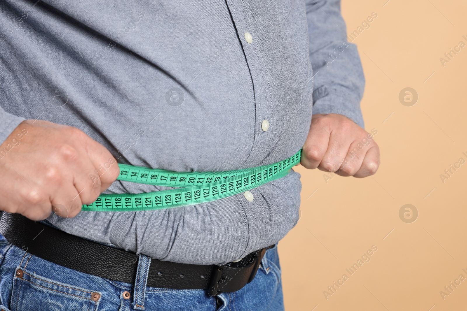 Photo of Overweight man measuring his belly with tape on beige background, closeup