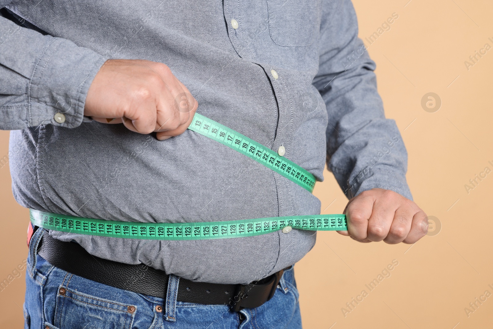 Photo of Overweight man measuring his belly with tape on beige background, closeup