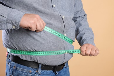 Photo of Overweight man measuring his belly with tape on beige background, closeup