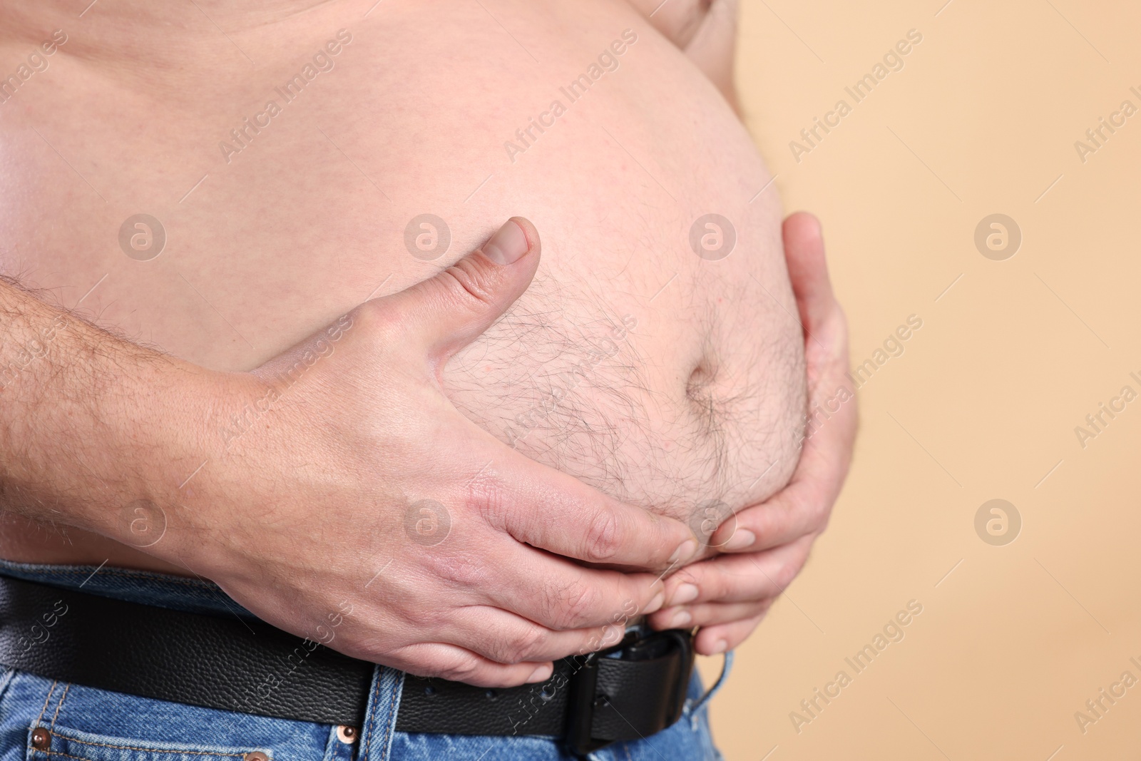 Photo of Overweight problem. Man with excessive belly fat on beige background, closeup