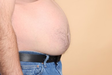 Photo of Overweight problem. Man with excessive belly fat on beige background, closeup. Space for text