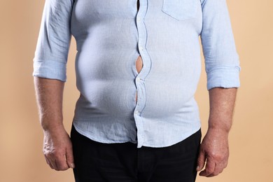 Photo of Overweight man in tight shirt on beige background, closeup