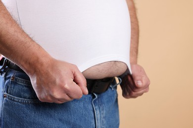 Photo of Overweight man in tight t-shirt on beige background, closeup