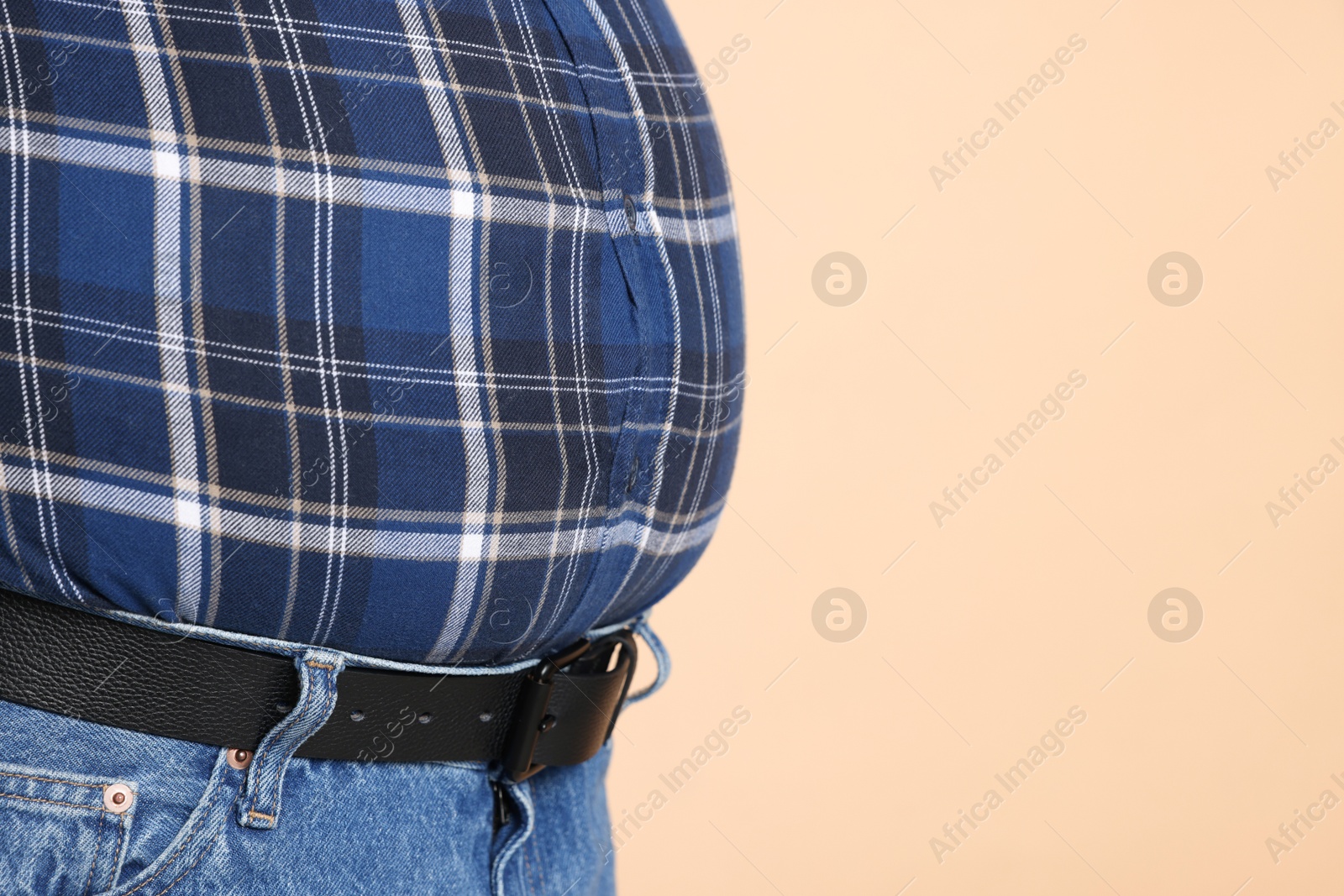 Photo of Overweight man in tight shirt on beige background, closeup. Space for text