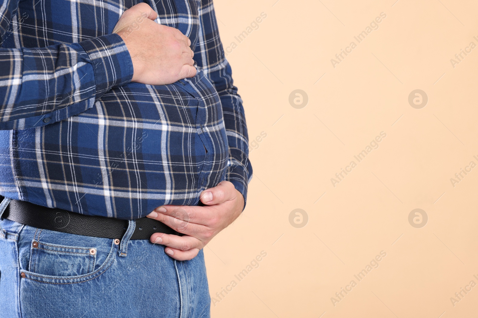 Photo of Overweight man in tight shirt on beige background, closeup. Space for text