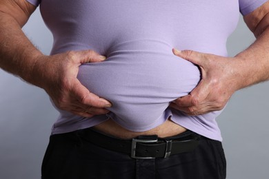 Photo of Overweight man in tight t-shirt on grey background, closeup