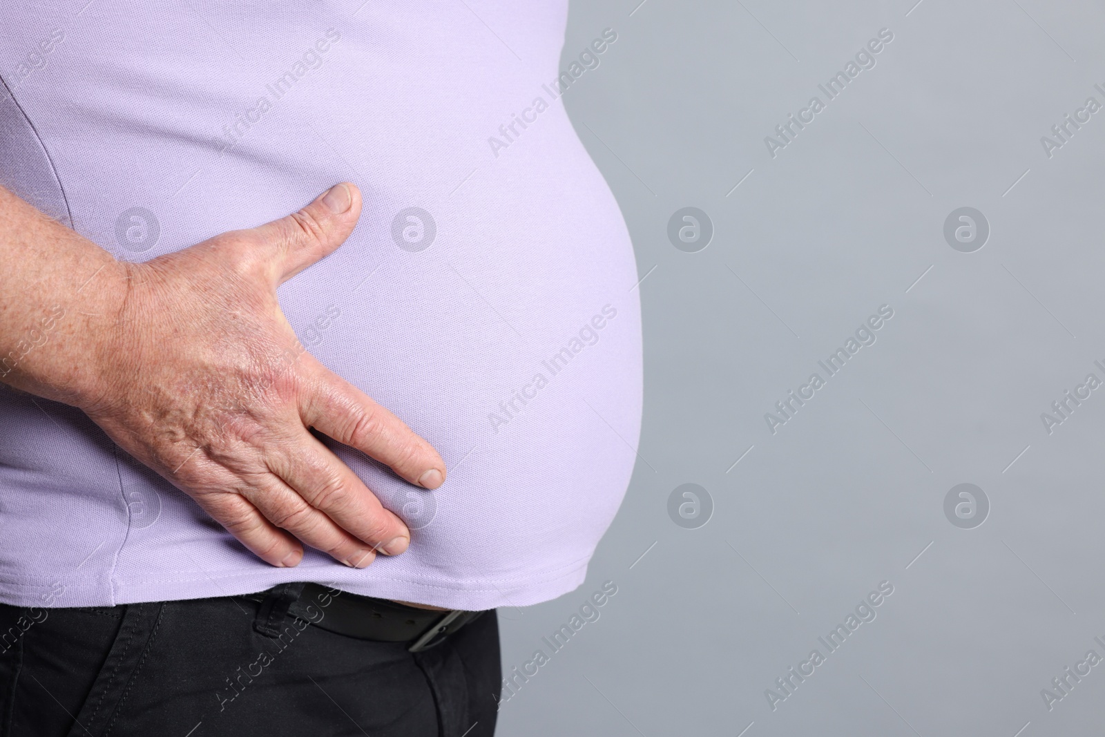 Photo of Overweight man in tight t-shirt on grey background, closeup. Space for text