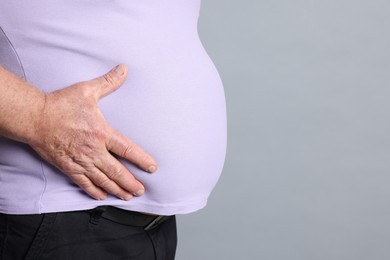 Photo of Overweight man in tight t-shirt on grey background, closeup. Space for text