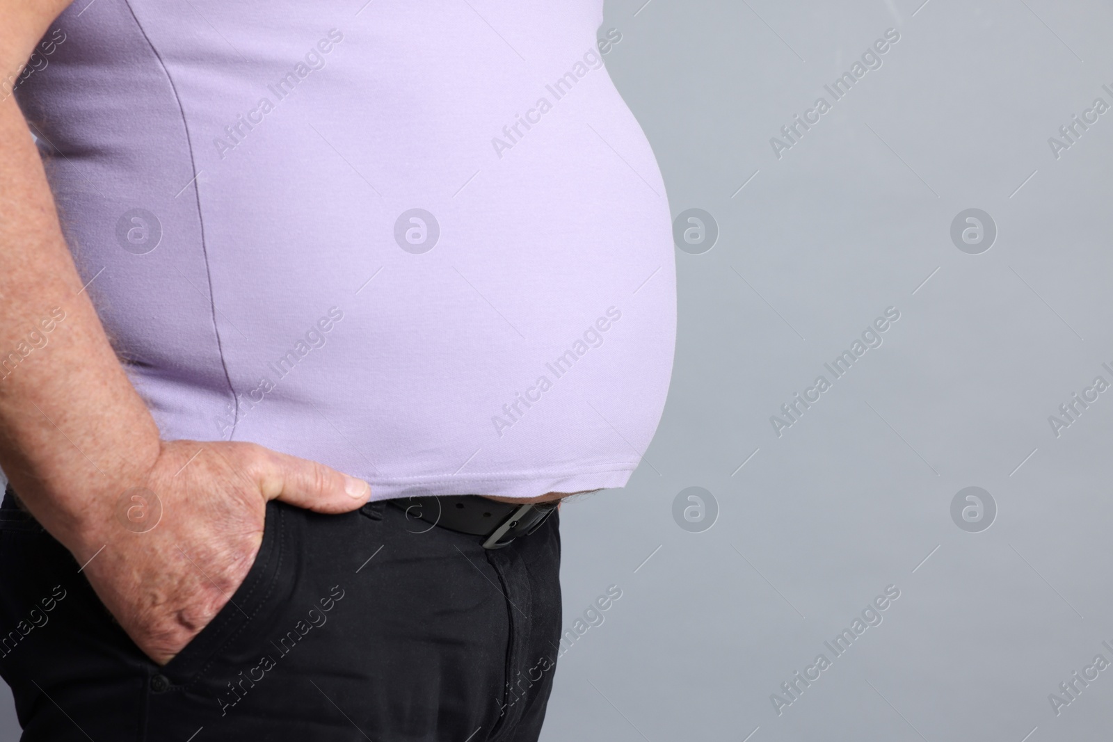 Photo of Overweight man in tight t-shirt on grey background, closeup. Space for text