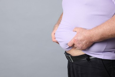 Photo of Overweight man in tight t-shirt on grey background, closeup. Space for text