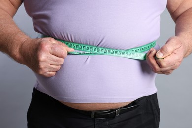 Photo of Overweight man measuring his belly with tape on grey background, closeup