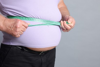 Photo of Overweight man measuring his belly with tape on grey background, closeup. Space for text