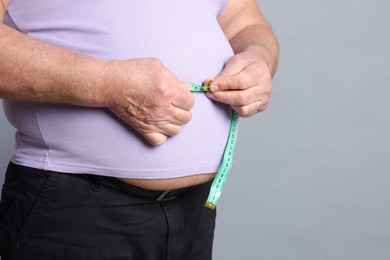 Photo of Overweight man measuring his belly with tape on grey background, closeup. Space for text