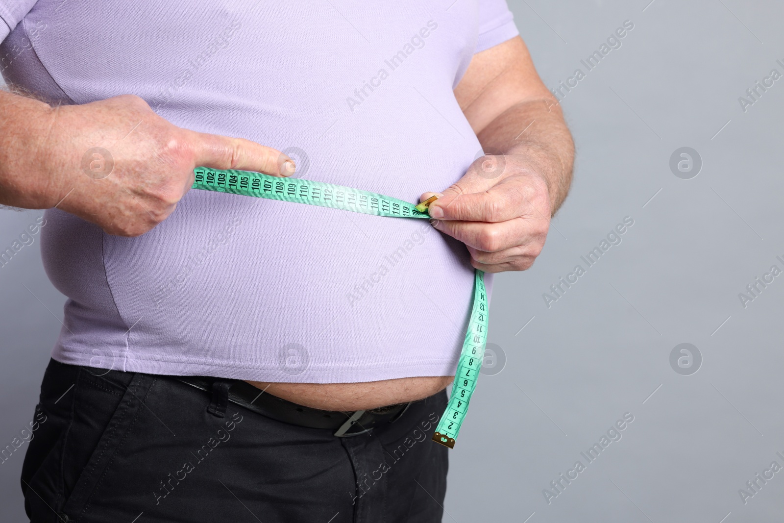 Photo of Overweight man measuring his belly with tape on grey background, closeup. Space for text