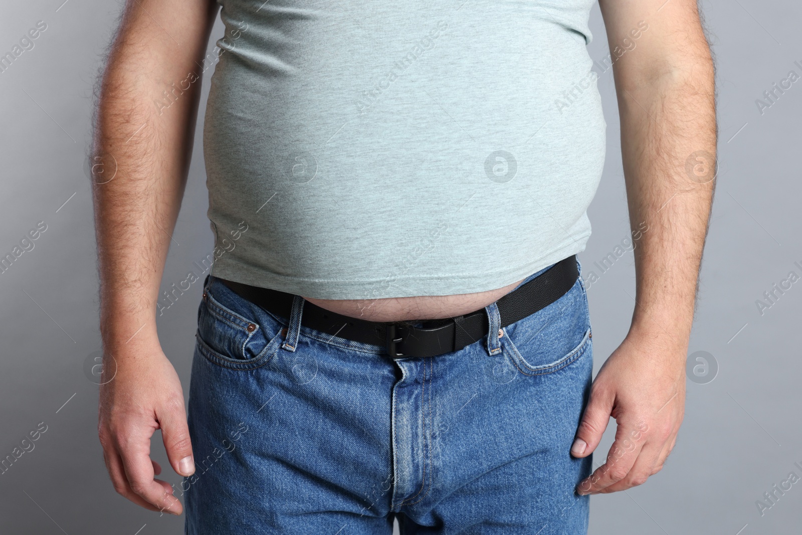 Photo of Overweight man in tight t-shirt on grey background, closeup