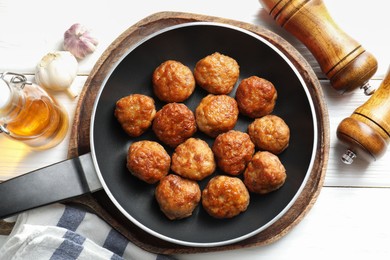 Photo of Tasty meatballs in frying pan and ingredients on white wooden table, flat lay