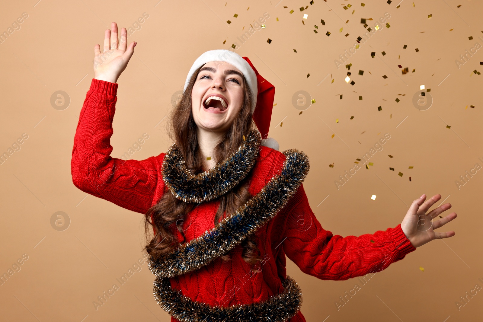 Photo of Happy young woman with tinsel under falling confetti on beige background