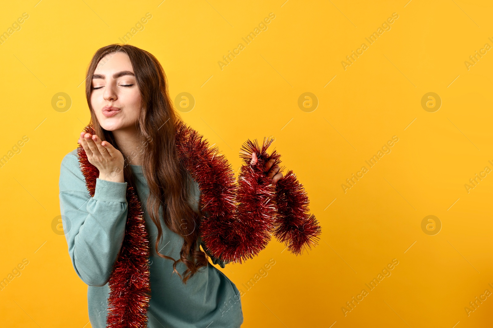 Photo of Young woman with tinsel blowing kiss on orange background. Space for text