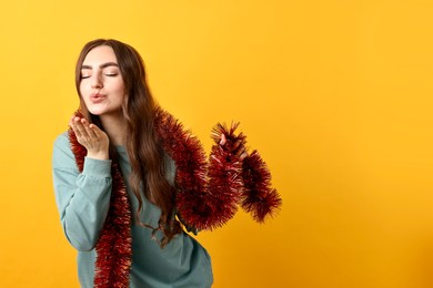 Photo of Young woman with tinsel blowing kiss on orange background. Space for text