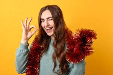 Photo of Young woman with tinsel showing OK gesture on orange background