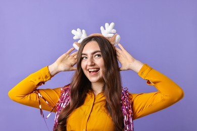 Photo of Happy young woman in reindeer headband with tinsel on purple background