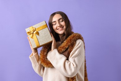 Photo of Happy young woman with tinsel and gift box on purple background