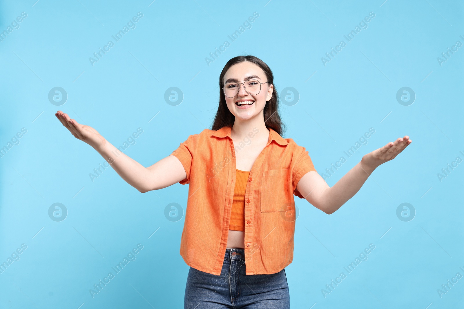 Photo of Happy woman welcoming friends or guests on light blue background