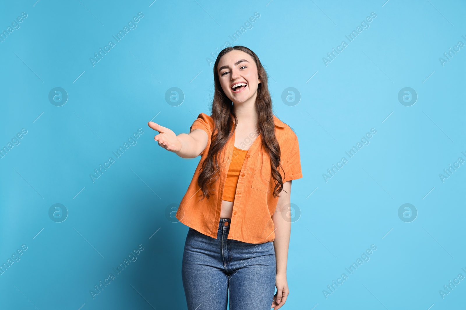 Photo of Happy woman welcoming friends or guests on light blue background