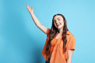 Photo of Happy woman welcoming friends or guests on light blue background. Space for text