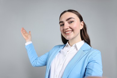 Photo of Happy businesswoman taking selfie and welcoming clients or partners on grey background