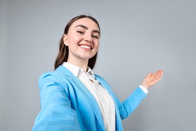 Photo of Happy businesswoman taking selfie and welcoming clients or partners on grey background