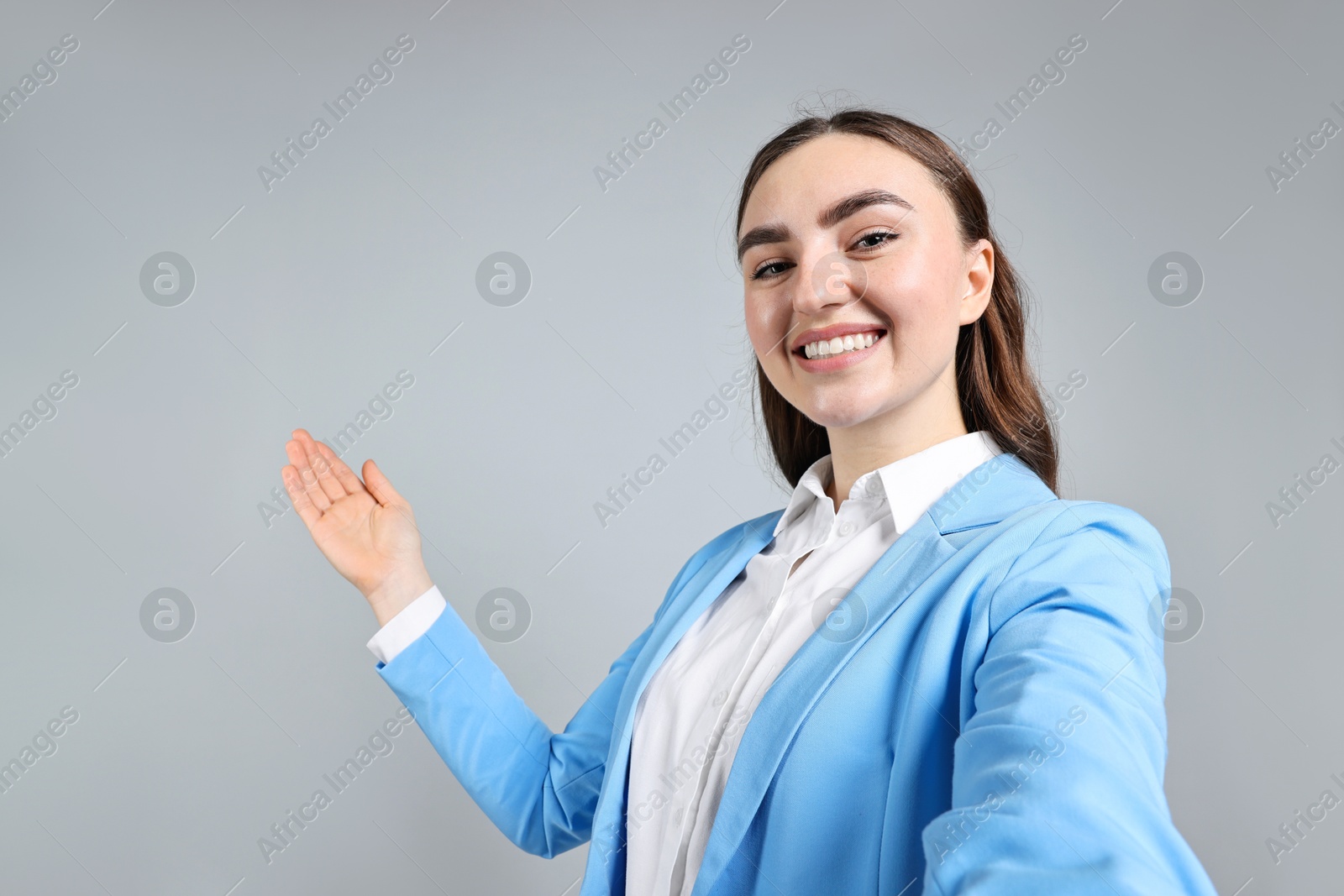 Photo of Happy businesswoman taking selfie and welcoming clients or partners on grey background