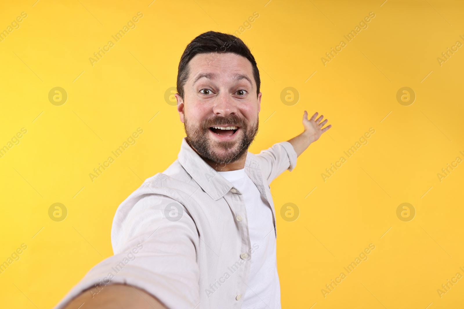 Photo of Happy man welcoming friends or guests on yellow background, view through front camera of gadget