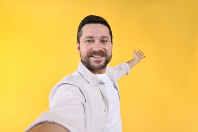 Photo of Happy man welcoming friends or guests on yellow background, view through front camera of gadget