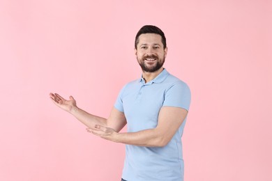 Photo of Happy man welcoming friends or guests on pink background