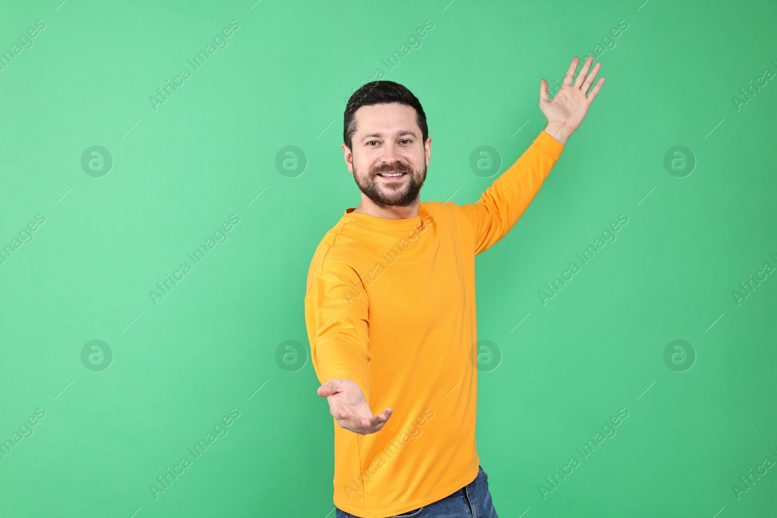 Photo of Happy man welcoming friends or guests on green background