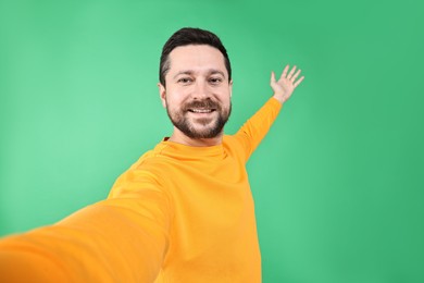 Photo of Happy man welcoming friends or guests by video call on green background, view through camera