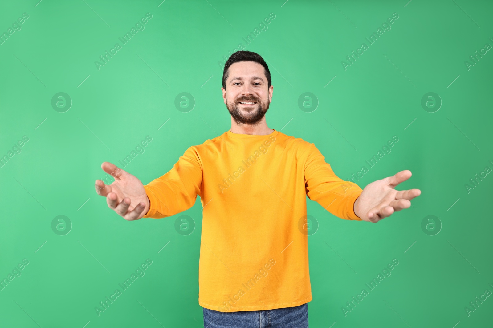 Photo of Happy man welcoming friends or guests on green background