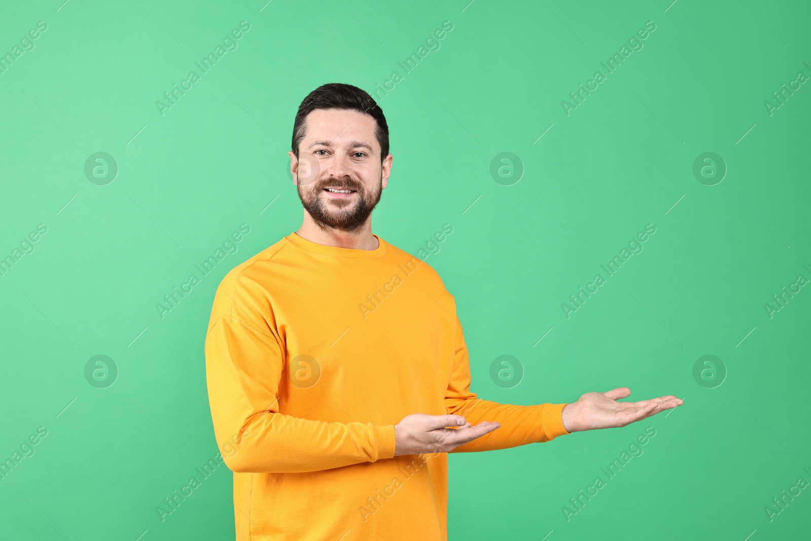 Photo of Happy man welcoming friends or guests on green background