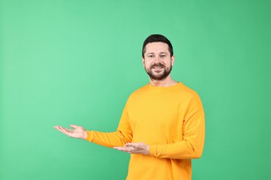 Photo of Happy man welcoming friends or guests on green background