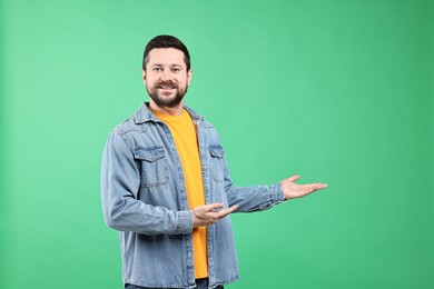 Photo of Happy man welcoming friends or guests on green background